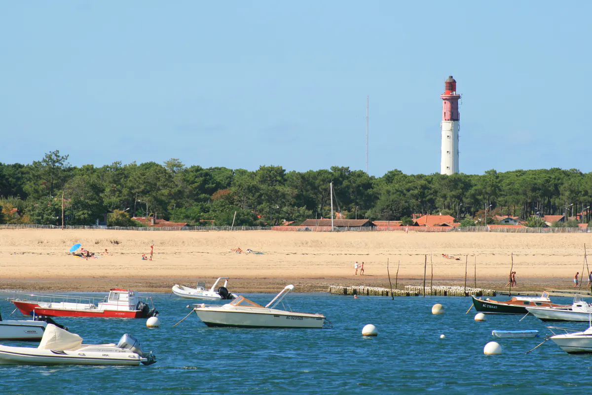 Phare rouge et blanc du Cap Ferret dominant la plage et les bateaux au mouillage