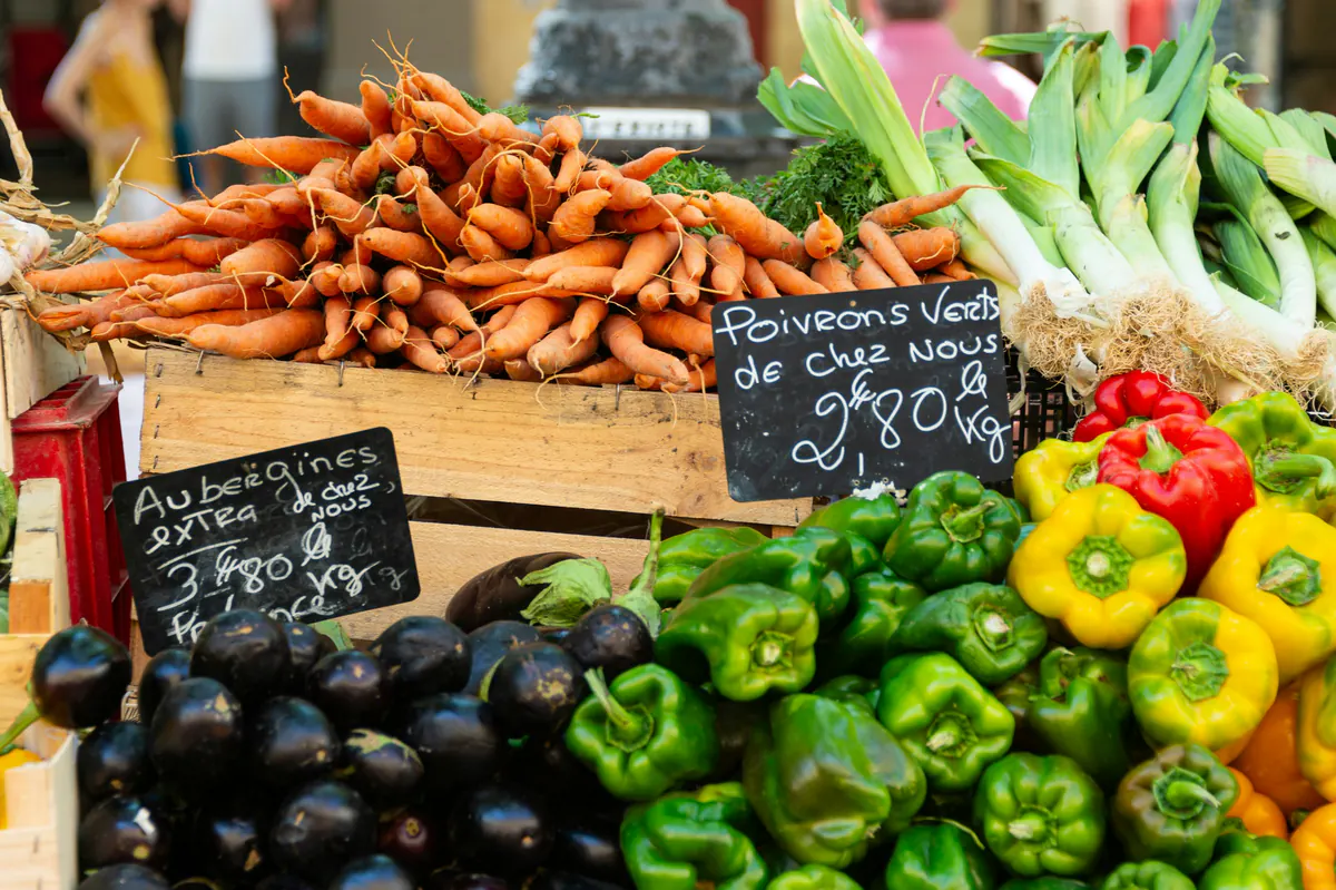 Étal de légumes de saison et ardoises de prix sur un marché provençal