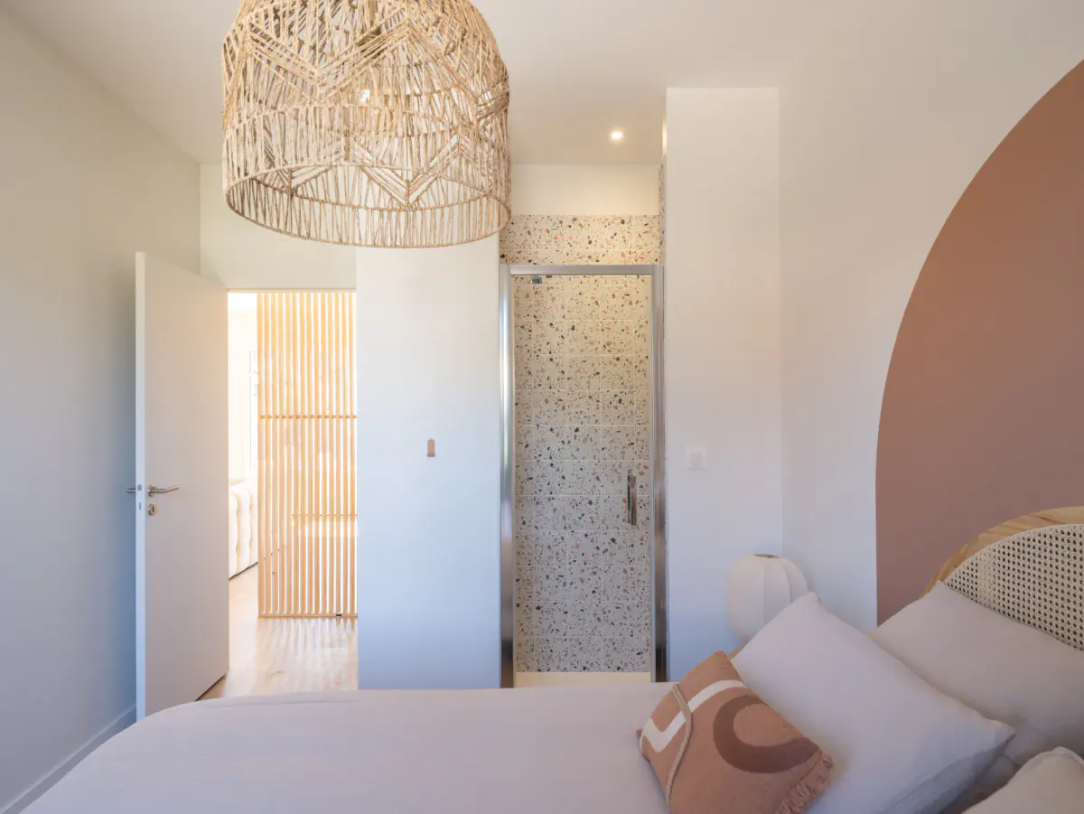 Chambre de Côté Pins : tête de lit cannée sur arche terracotta, suspension en raphia et douche en terrazzo