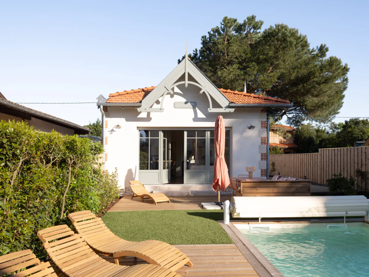 Maison Côté Pins face à la piscine, transats en bois sur la terrasse et grand pin parasol
