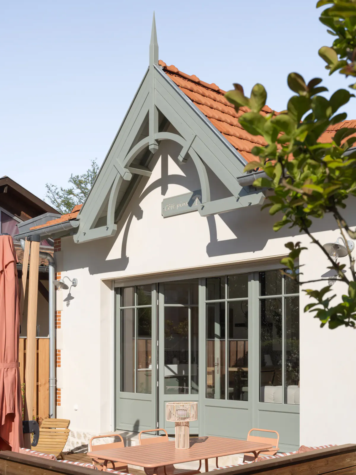 Pignon à lambrequins de la maison Côté Pins et sa plaque, au-dessus de la table de terrasse