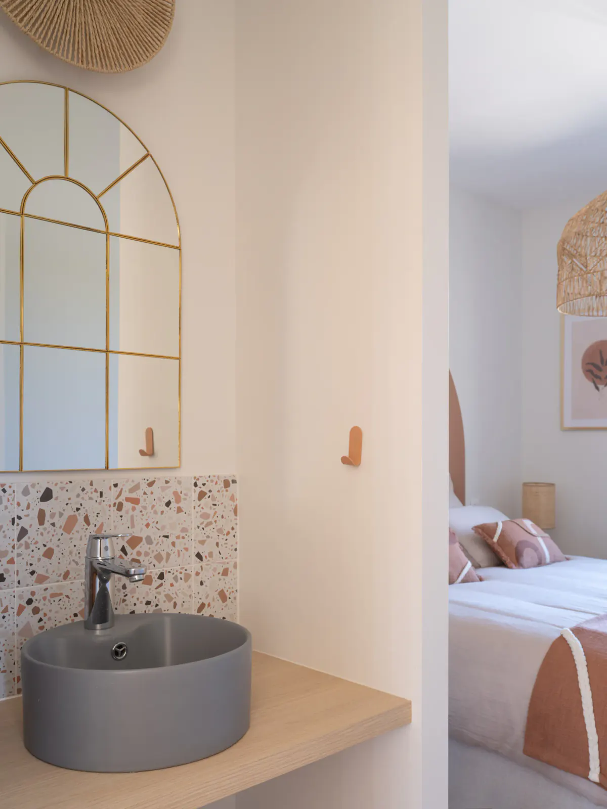 Vasque grise et miroir arche doré, chambre aux tons terracotta en arrière-plan